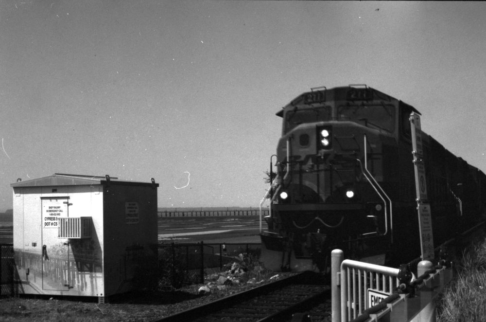 A BNSF locomotive approaching a level crossing beside the sea, tide out, pier in the distance