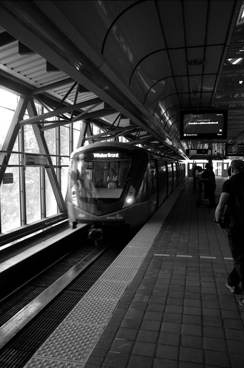 A SkyTrain arriving at an elevated platform, motion-blurred, destination sign reading Waterfront