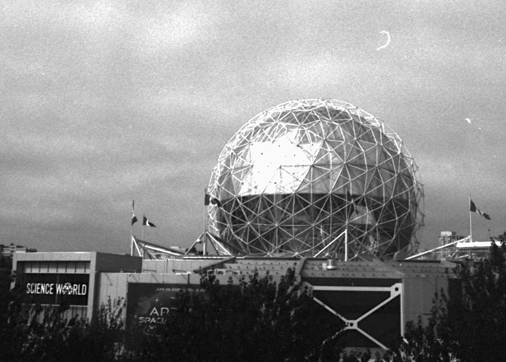 The geodesic dome of Science World against a grey sky, a thin crescent moon above it