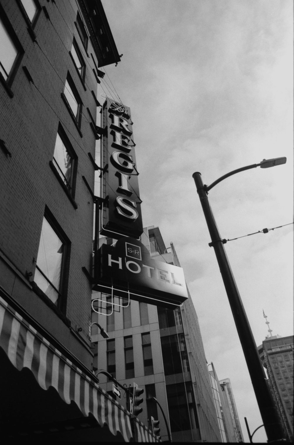 The vertical neon sign of the St Regis Hotel photographed from below against a bright sky