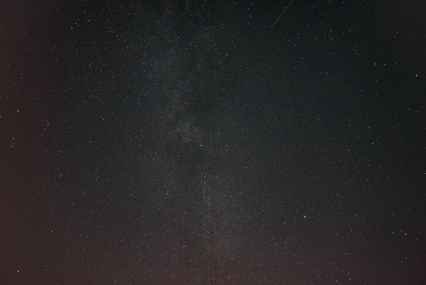 The band of the Milky Way across a dense starfield, with a faint meteor trail crossing the upper right